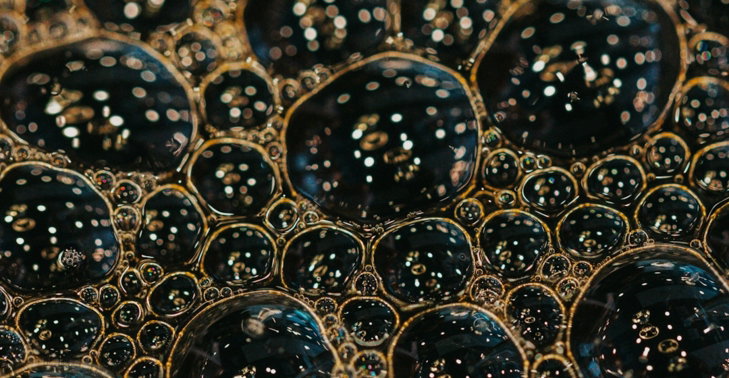 Dark bubbles with golden reflections on a liquid surface.