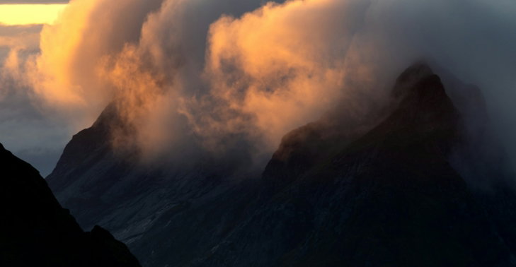 Clouds glowing with golden light clinging to dark mountain peaks at low sun.